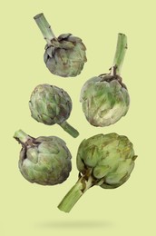 Image of Fresh raw artichokes falling on green background