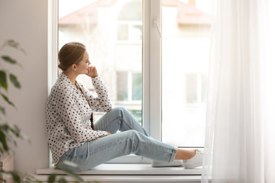 Beautiful young woman looking out of window at home