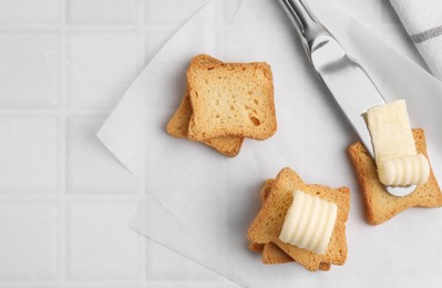 Photo of Tasty butter curls, knife and pieces of dry bread on white tiled table, flat lay. Space for text