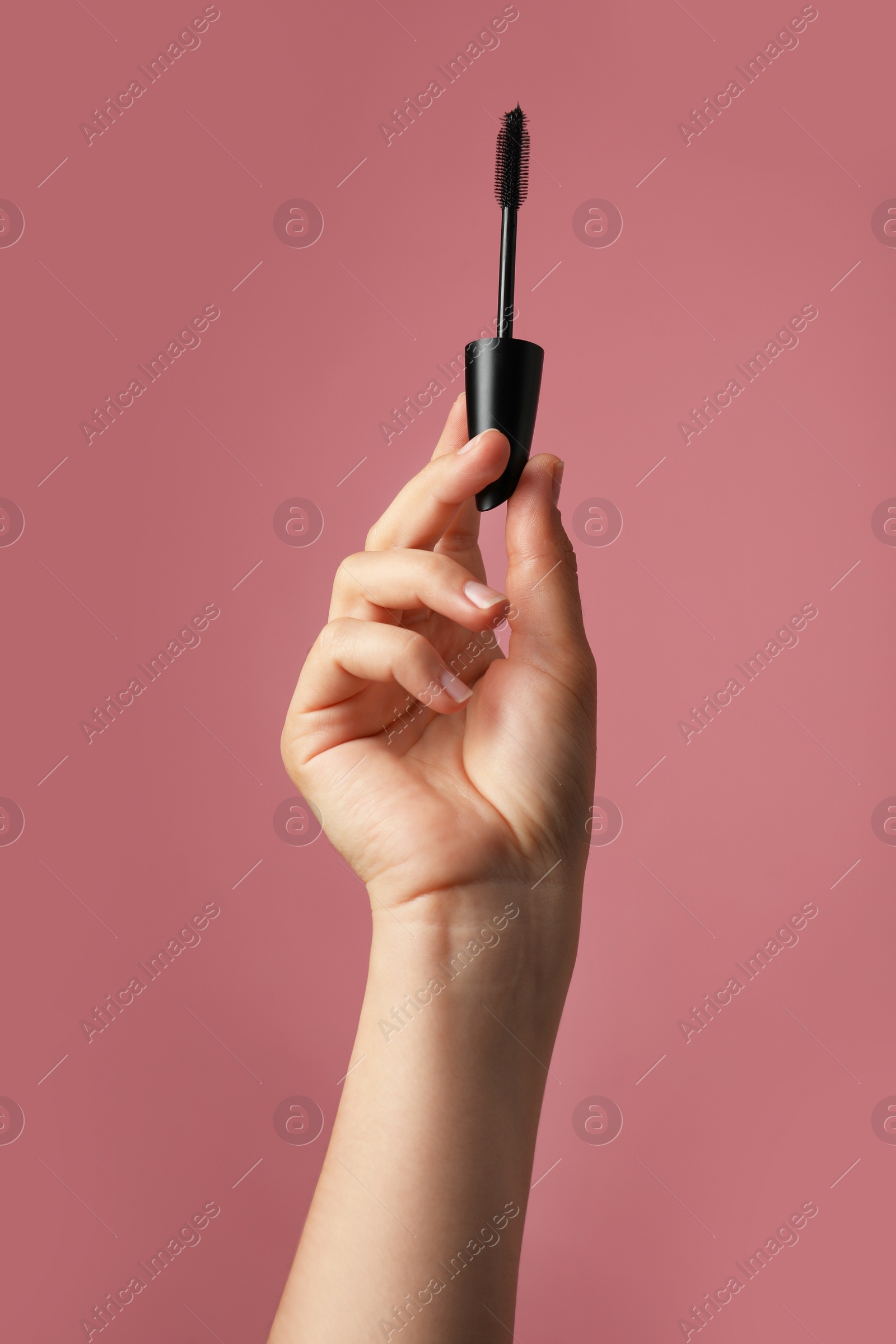 Photo of Woman holding mascara for eyelashes on dusty rose background, closeup