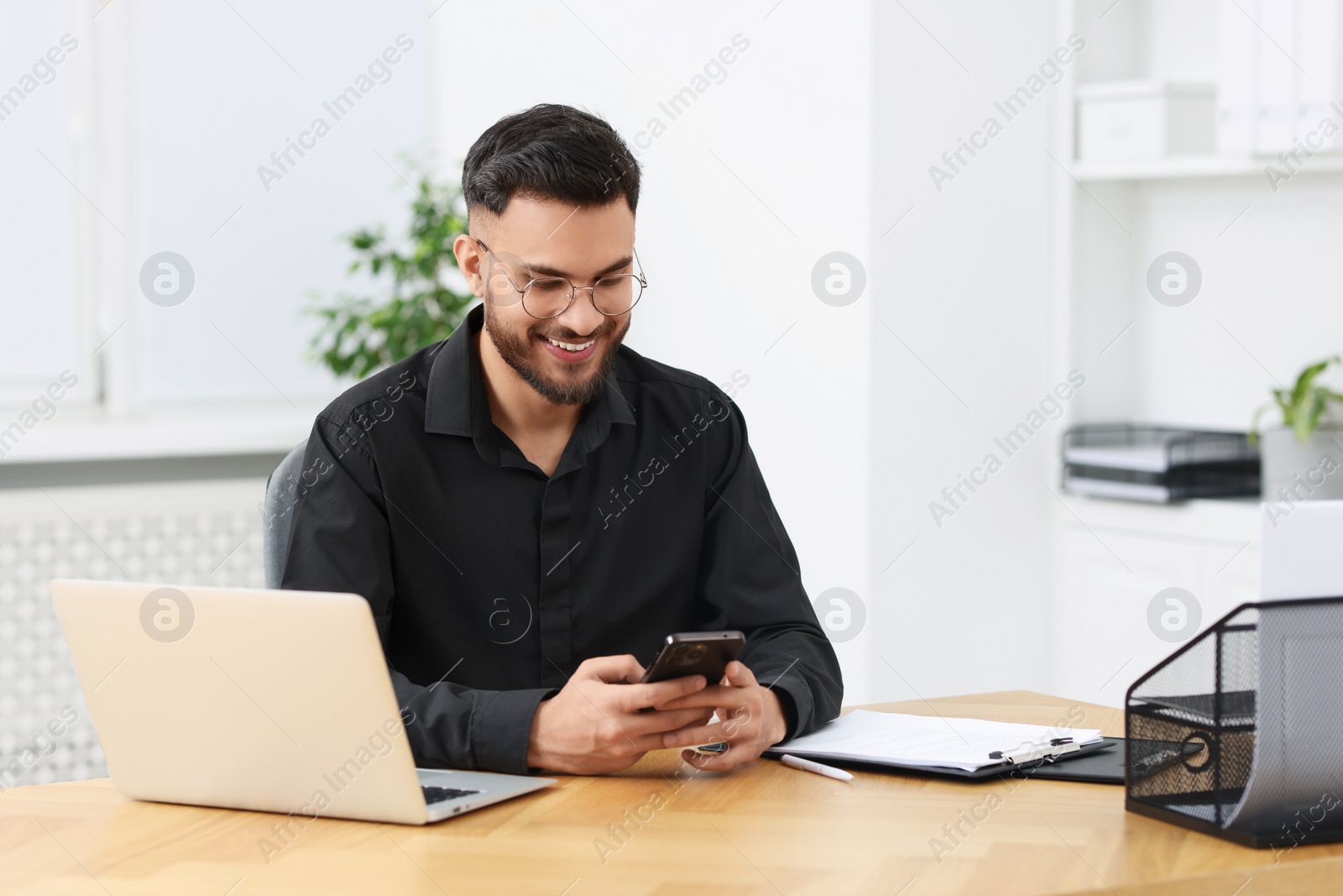 Photo of Handsome young man using smartphone at wooden table in office