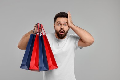 Photo of Shocked man with many paper shopping bags on grey background