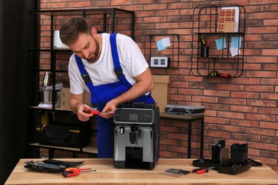 Photo of Repairman with screwdriver fixing coffee machine at table indoors