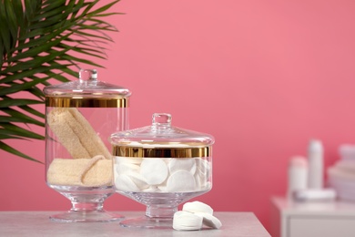 Composition of glass jars with cotton pads on table against pink background. Space for text