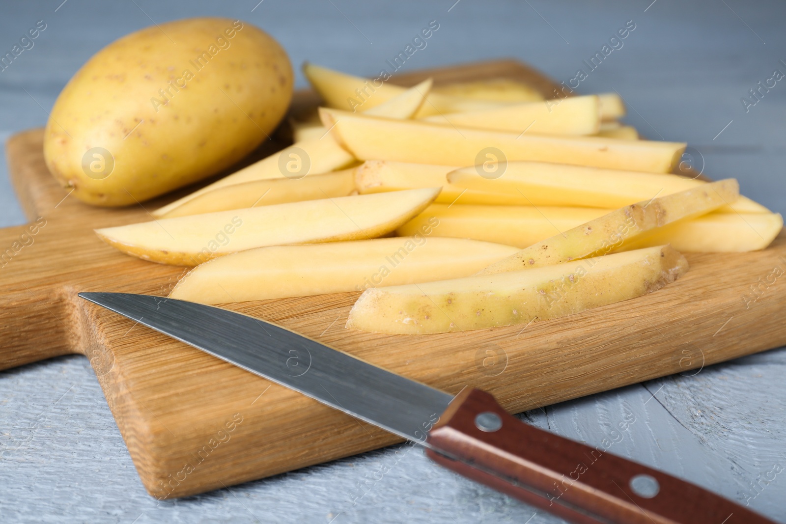 Photo of Whole and cut potatoes with knife on grey wooden table, closeup. Cooking delicious french fries