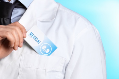 Doctor putting business card into pocket on color background, closeup. Medical service