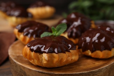 Photo of Delicious profiteroles with chocolate spread and mint on wooden board, closeup