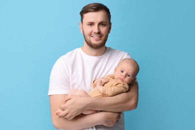 Father with his cute baby on light blue background