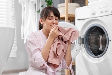 Young housewife with laundry near washing machine at home