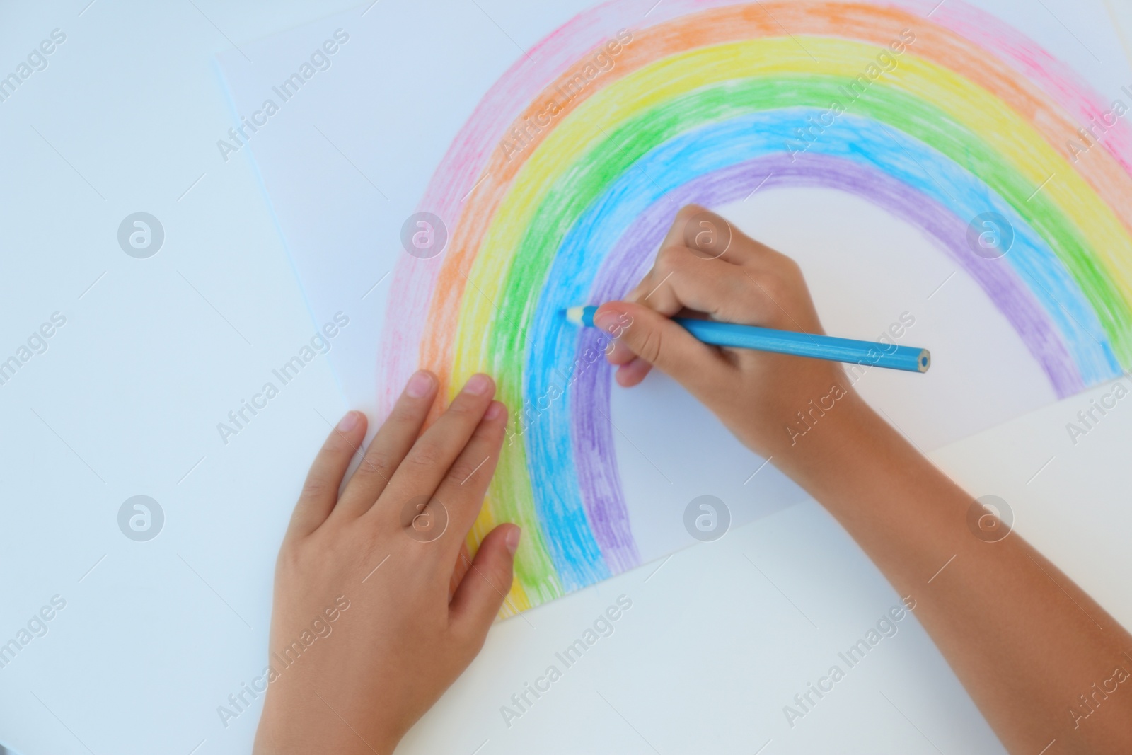 Photo of Little child drawing rainbow on white background, top view. Stay at home concept