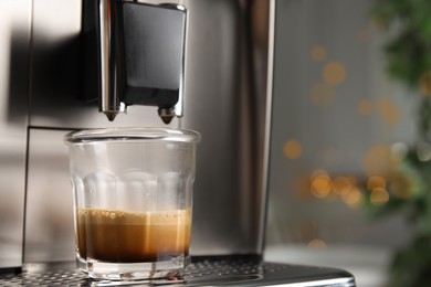 Photo of Espresso machine with glass of fresh coffee on drip tray against blurred background, closeup. Space for text