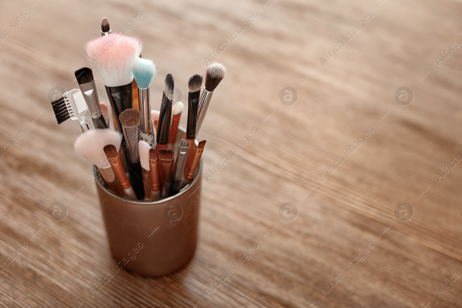 Photo of Holder with makeup brushes on wooden table