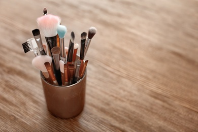 Holder with makeup brushes on wooden table