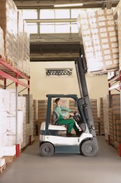 Photo of Worker sorting cardboard boxes with forklift truck in warehouse. Logistics concept