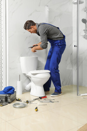 Professional plumber working with toilet bowl in bathroom