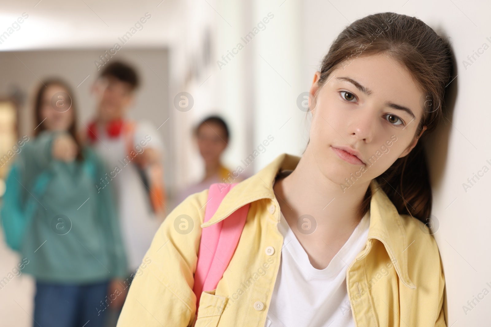 Photo of Teen problems. Lonely girl standing separately from other students at school