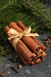 Photo of Different spices. Aromatic cinnamon sticks, clove seeds and fir branches on dark gray textured table, closeup