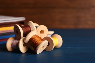 Photo of Set of color sewing threads on blue wooden table, space for text