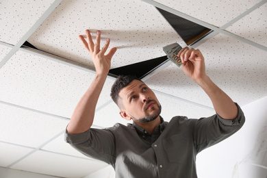 Photo of Man hiding money under ceiling cell indoors. Financial savings