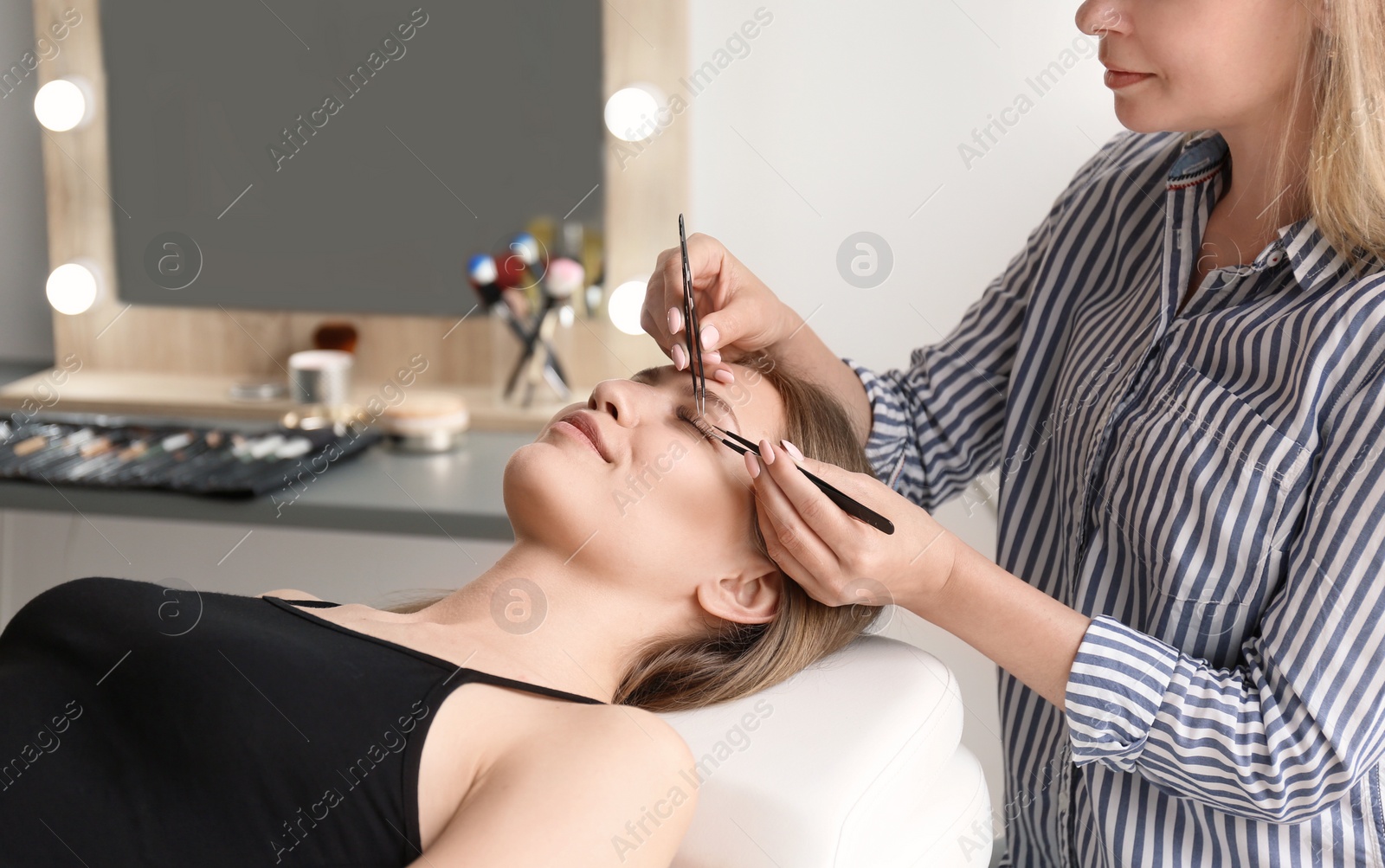 Photo of Young woman undergoing eyelash extensions procedure in salon