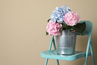 Beautiful hortensia flowers in bucket on chair near beige wall. Space for text