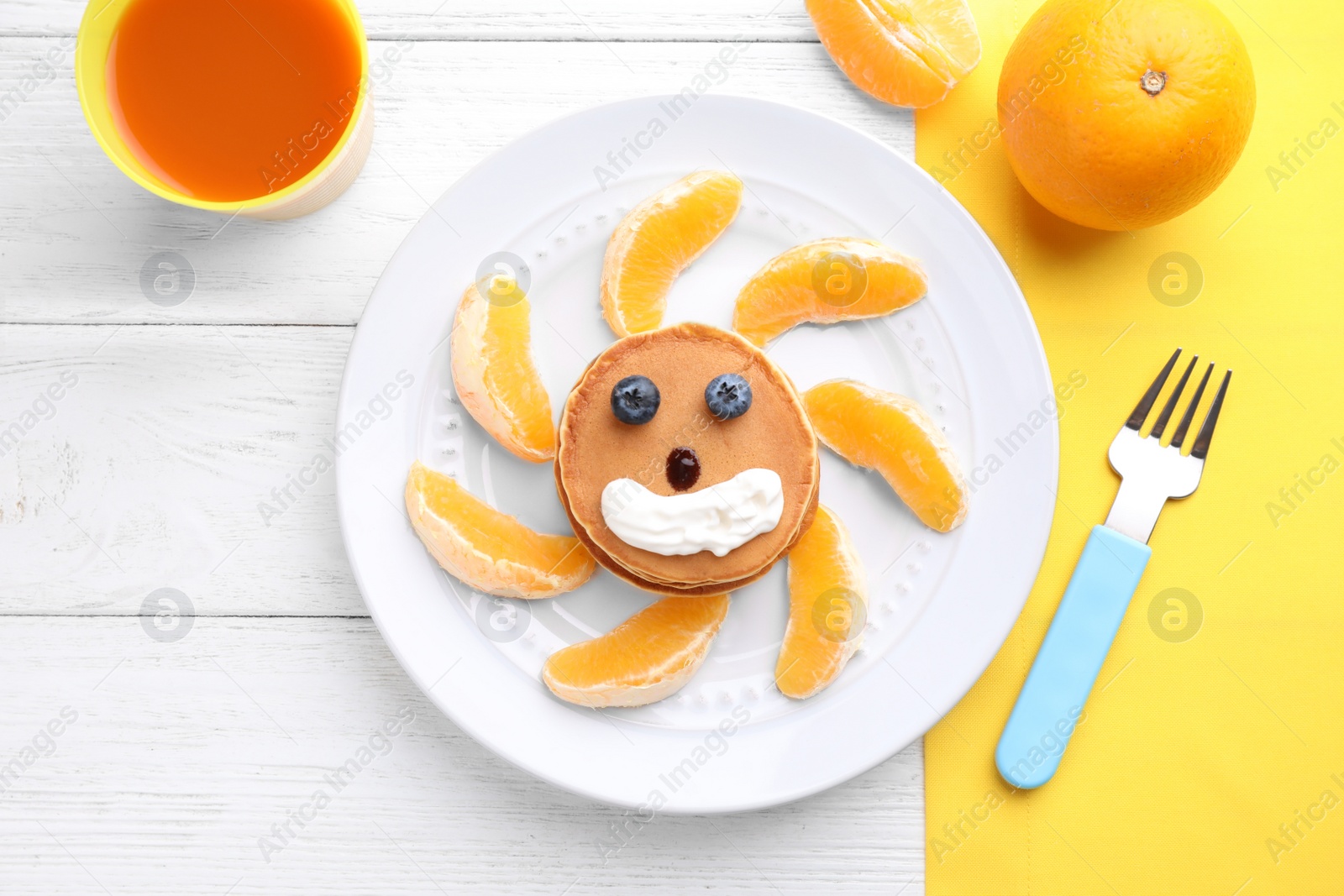 Photo of Tasty pancakes served with orange, whipped cream and juice on white wooden table, flat lay. Creative idea for kids breakfast