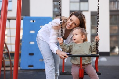 Happy nanny and cute little boy on swing outdoors