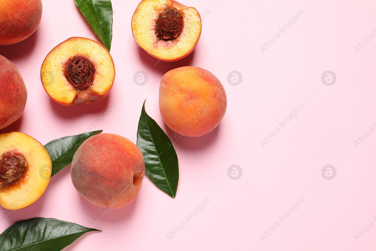 Photo of Cut and whole fresh ripe peaches with green leaves on pink background, flat lay. Space for text