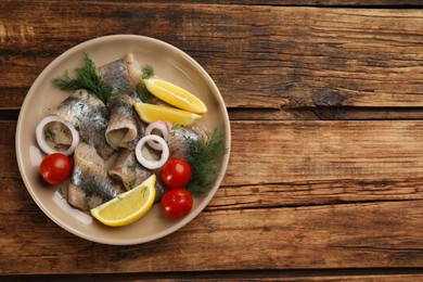 Salted herring fillets served with lemon, cherry tomatoes and onion on wooden table, top view. Space for text