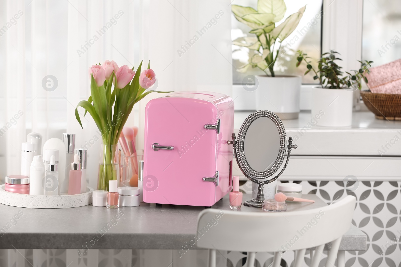 Photo of Pink mini cosmetics refrigerator and skin care products on table