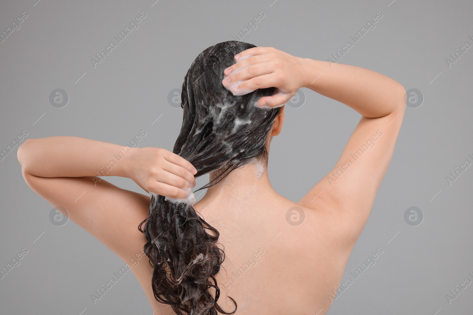 Photo of Woman washing hair on grey background, back view