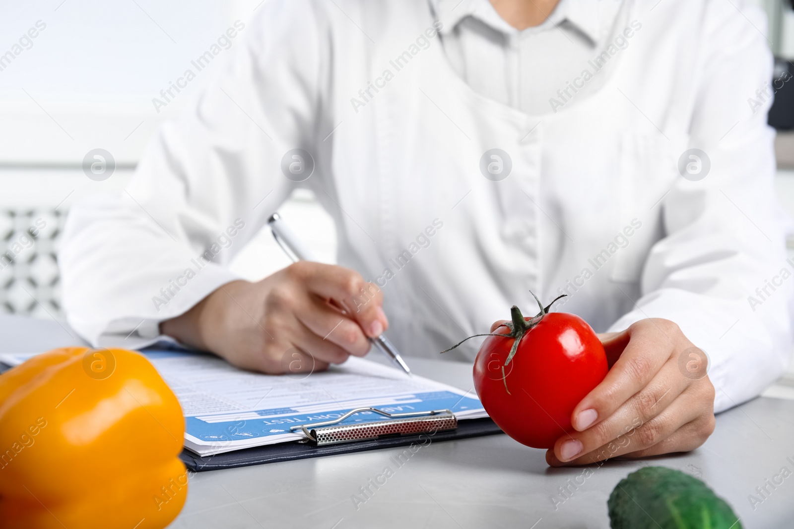 Photo of Scientist with laboratory test form and fresh tomato at table indoors, closeup. Poison detection