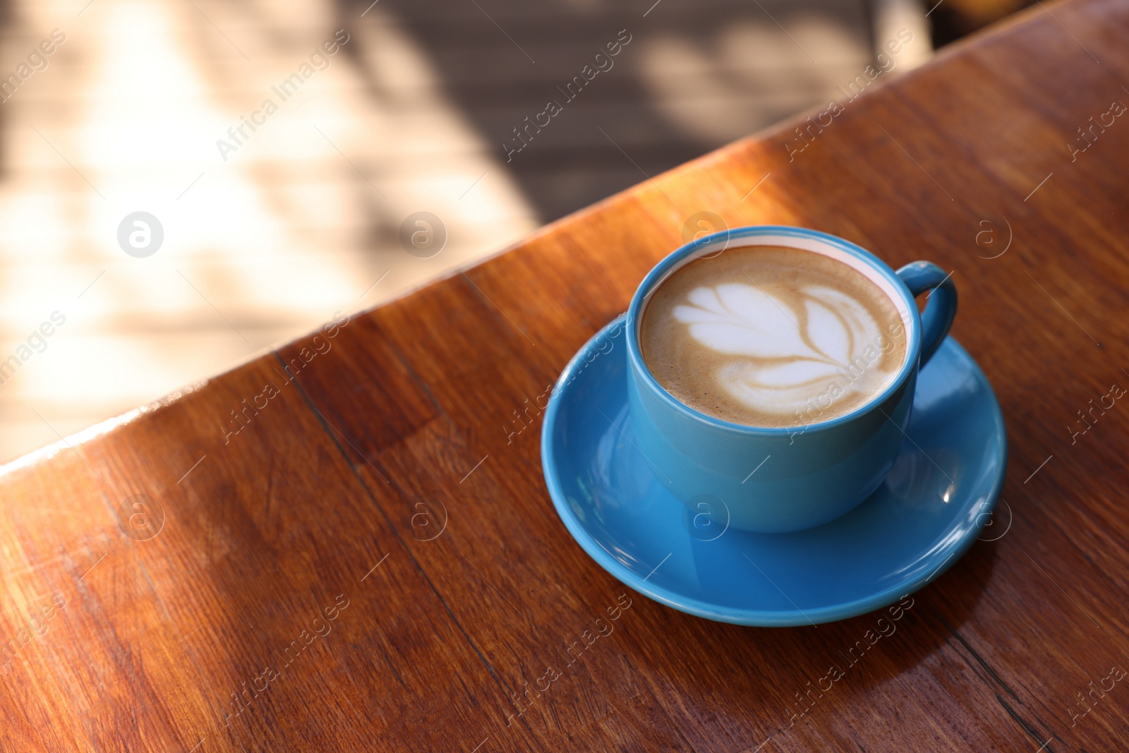 Photo of Ceramic cup of aromatic coffee with foam on wooden table in outdoor cafe. Space for text