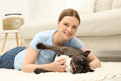 Photo of Happy woman playing with cute French Bulldog on soft carpet in room