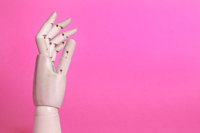 Wooden mannequin hand on pink background. Space for text