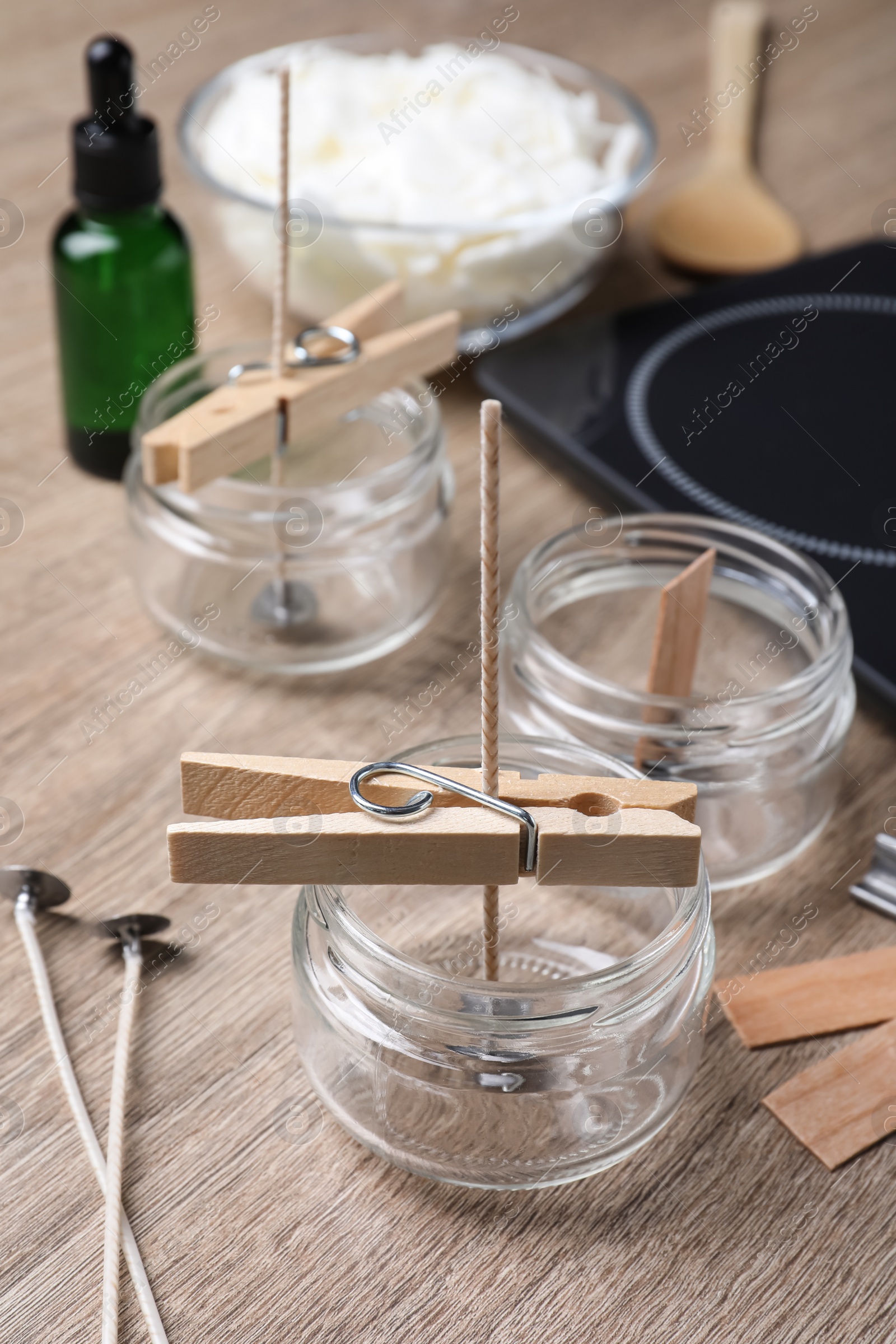 Photo of Glass jars with wicks and clothespins as stabilizers on wooden table. Making homemade candles