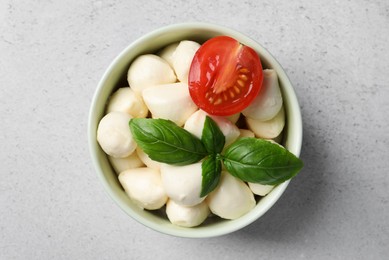 Photo of Delicious mozzarella balls in bowl, tomato and basil leaves on light gray table