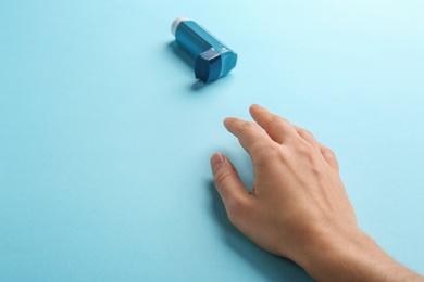 Woman reaching for asthma inhaler on color background, closeup. Space for text