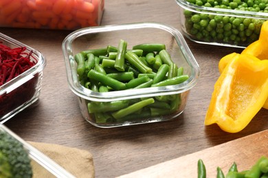 Containers with green beans and fresh products on wooden table. Food storage