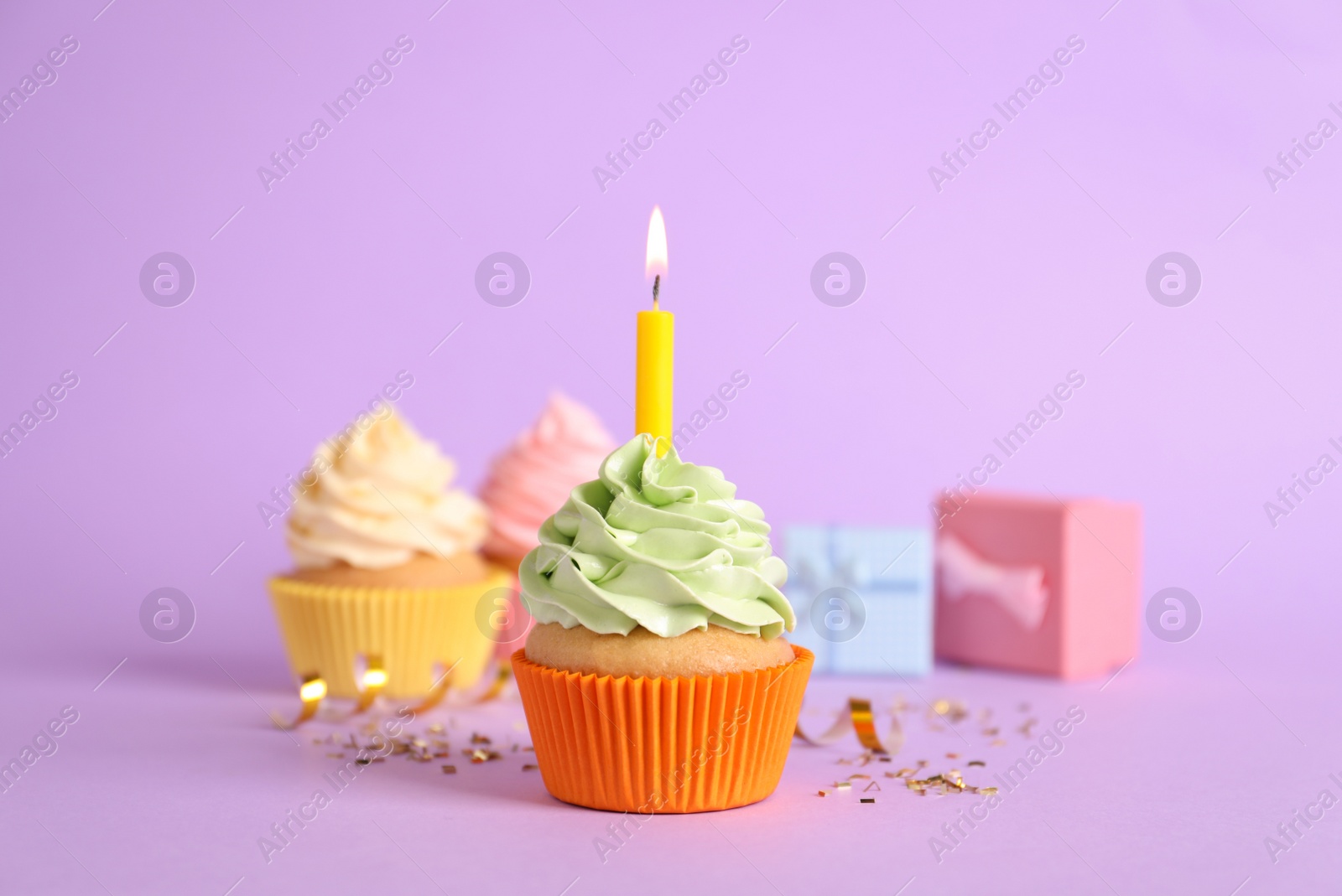 Photo of Birthday cupcake with burning candle and confetti on violet background