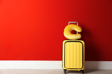 Photo of Yellow suitcase and travel pillow near red wall, space for text