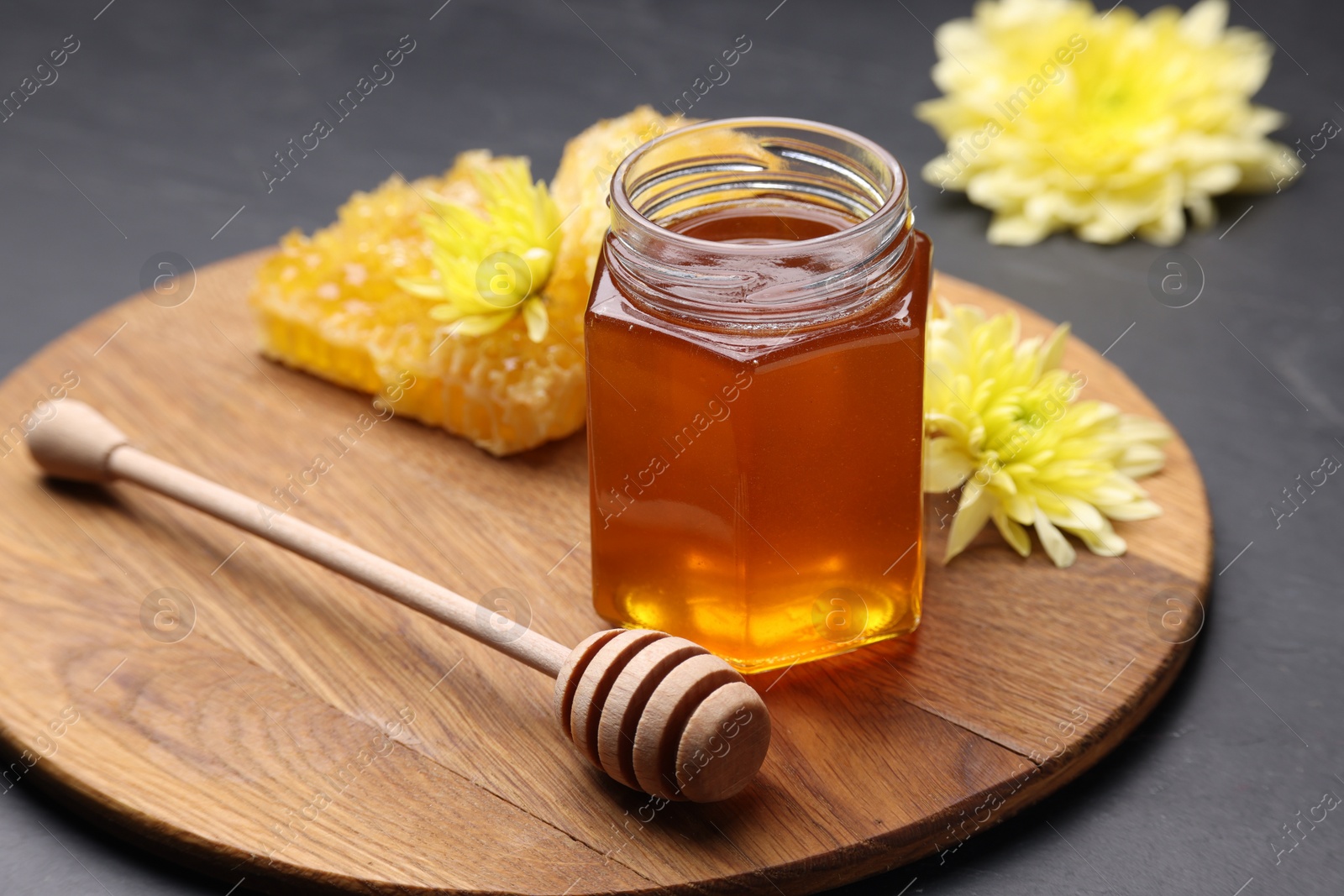 Photo of Sweet honey in jar, dipper and chrysanthemum flowers on grey table