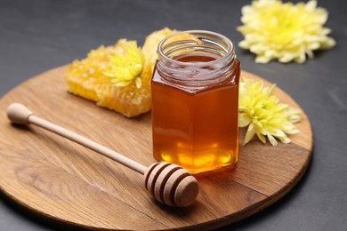 Photo of Sweet honey in jar, dipper and chrysanthemum flowers on grey table