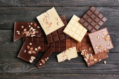 Photo of Different chocolate bars with nuts on wooden background, top view