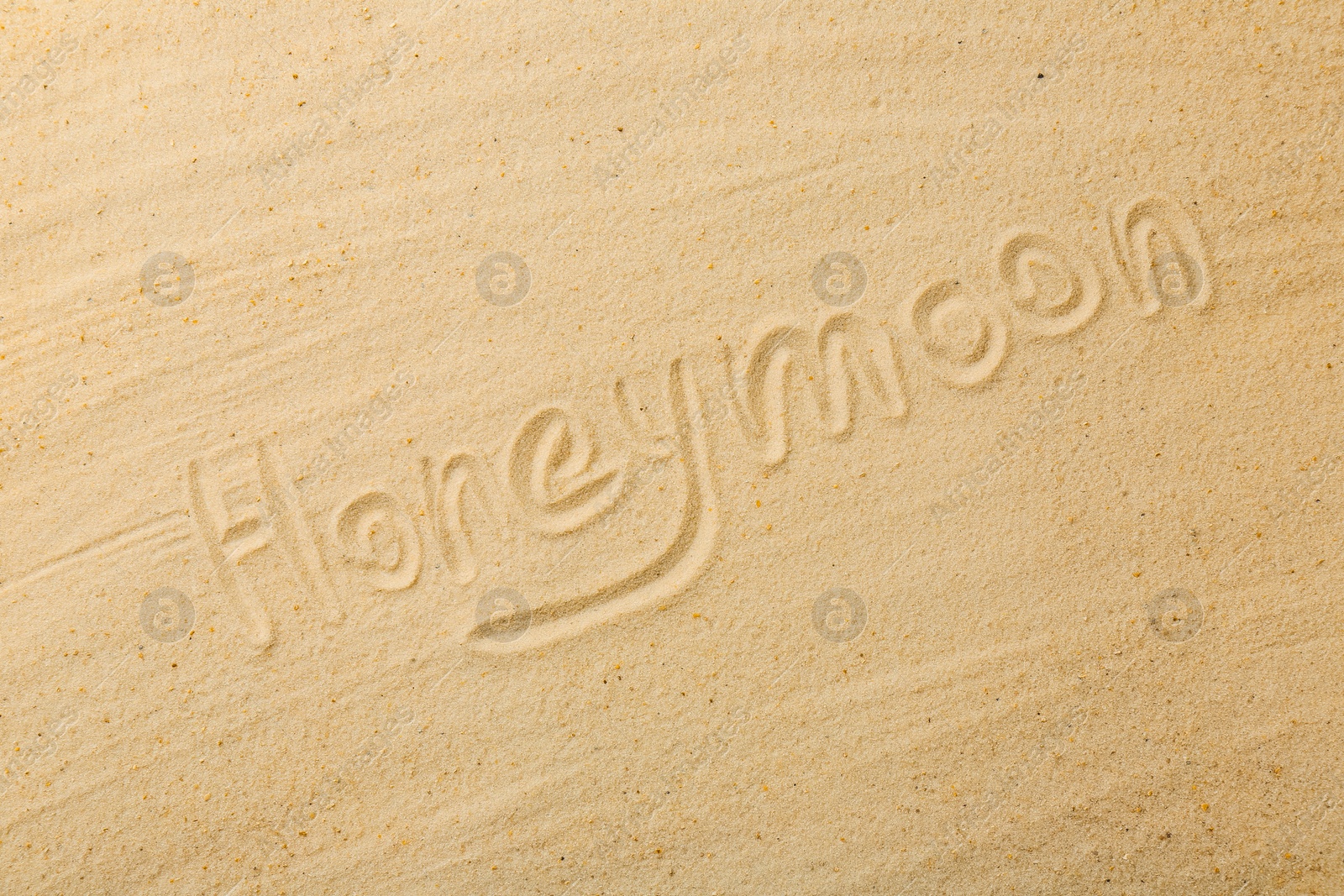 Photo of Word Honeymoon written on sand, top view