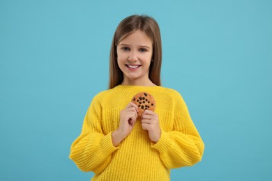 Photo of Cute girl with chocolate chip cookie on light blue background