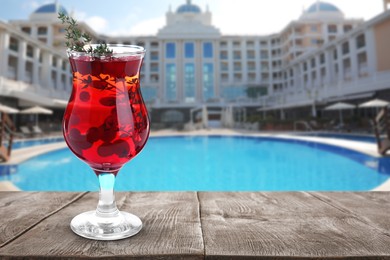 Tasty refreshing cocktail on wooden table near outdoor swimming pool at resort, space for text