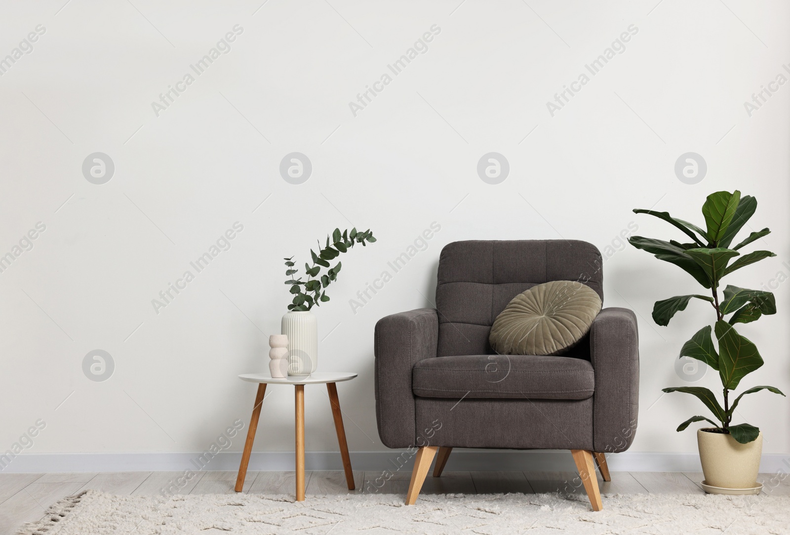 Photo of Comfortable armchair, pillow, side table and green houseplants indoors, space for text