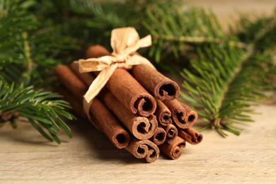 Bunch of cinnamon sticks and fir branches on wooden table, closeup