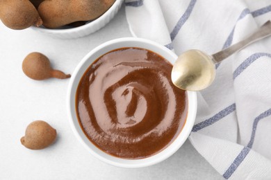 Photo of Bowl of tamarind sauce, spoon and fresh pods on light table, flat lay